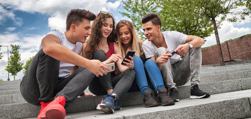 Vier Personen sitzen auf einer Steintreppe. Die Personen haben alle ein Handy in der Hand.