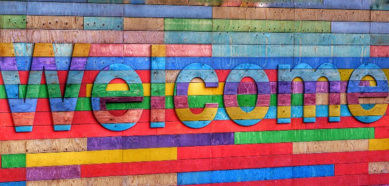 Auf einem bunten Hintergrund in vielen Regenbogenfarben steht reliefartig hervorgehoben das Wort "Welcome".