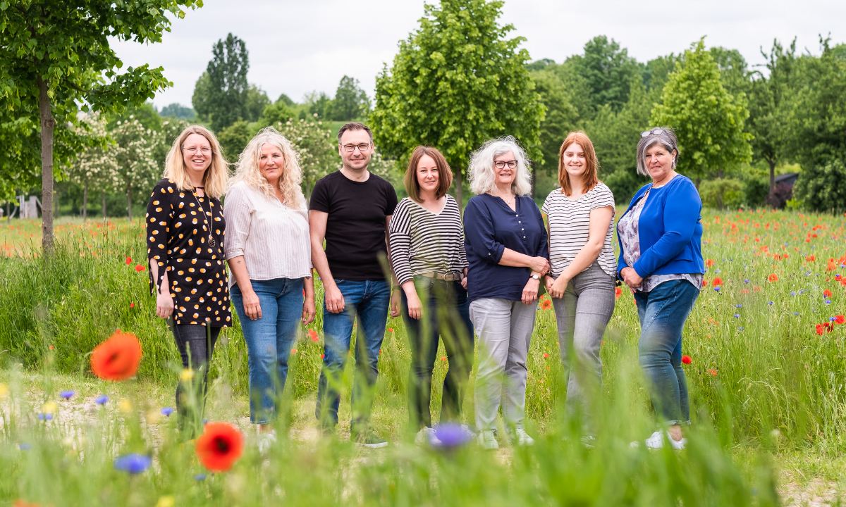 Sieben Personen aus dem Leitungsteam von Startklar Soziale Arbeit Niederbayern stehen auf einer sommerlichen Wiese nebeneinander und schauen zur Kamera.